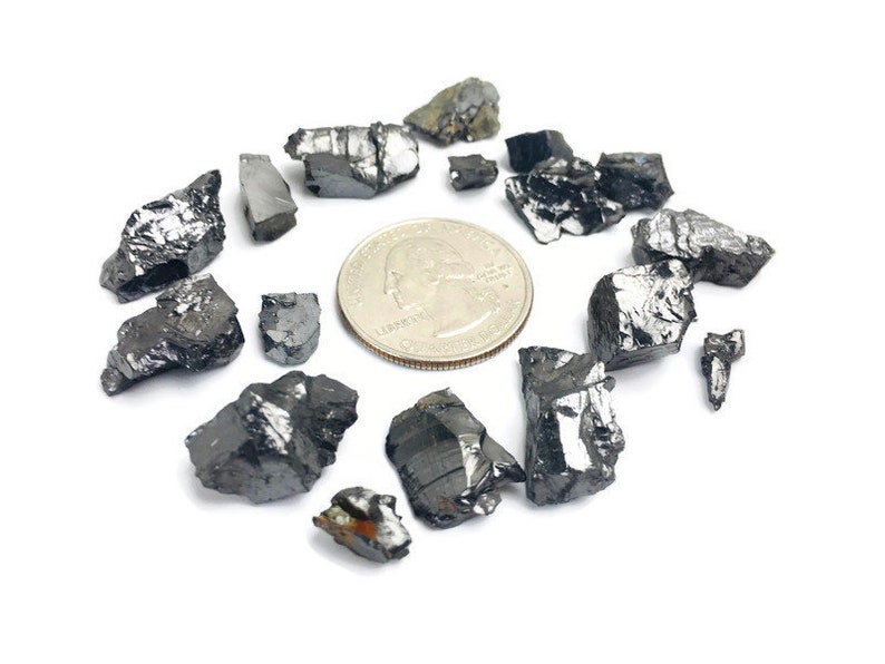 May include: A collection of black, irregularly shaped, rough-textured stones, some with a metallic sheen, scattered around a silver US quarter.