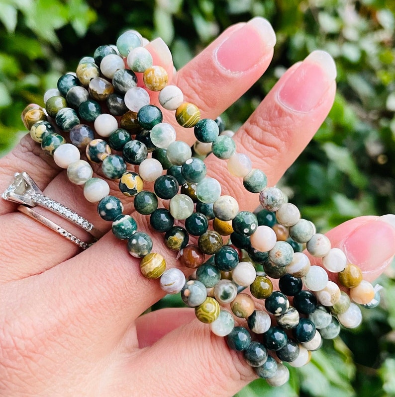 May include: A stack of green, brown, and white gemstone bracelets. The bracelets are made of small, round beads and are layered on top of each other.