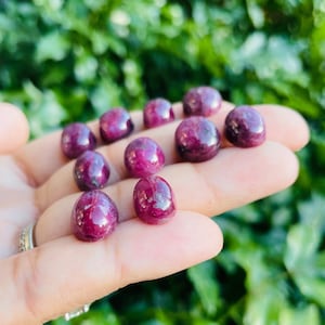 May include: A collection of ten small, round, cabochon-cut ruby gemstones. The rubies are a deep red color and have a smooth, polished finish.