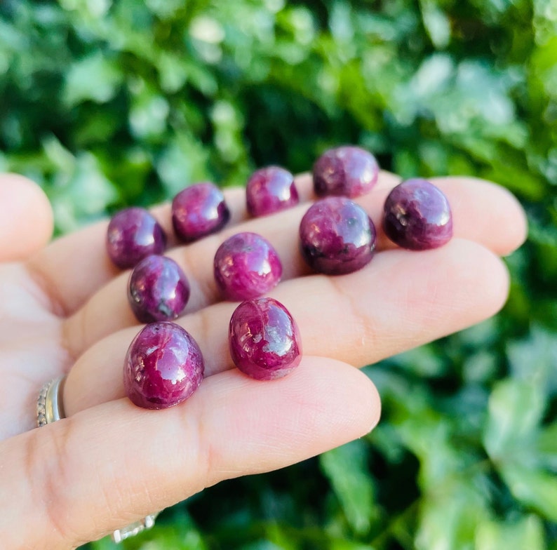 May include: A collection of ten small, round, cabochon-cut ruby gemstones. The rubies are a deep red color and have a smooth, polished finish.