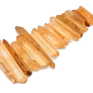 May include: A collection of 15 raw, pointed, orange-brown quartz crystals, also known as citrine, arranged in a staggered pattern.