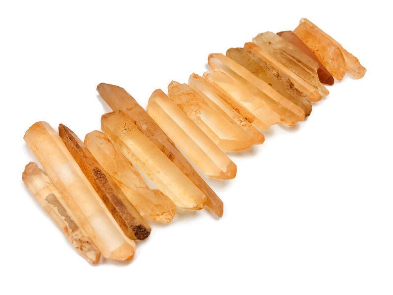 May include: A collection of 15 raw, pointed, orange-brown quartz crystals, also known as citrine, arranged in a staggered pattern.