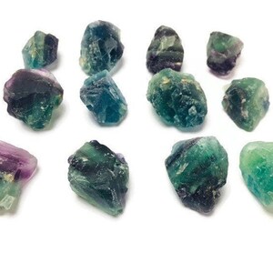 Pu&ograve; includere: Una collezione di 12 cristalli di fluorite di colore verde, blu e viola. I cristalli sono grezzi e hanno una variet&agrave; di forme e dimensioni.