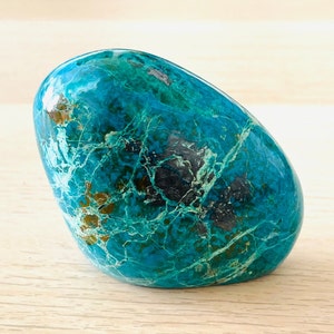 May include: A smooth, polished blue-green gemstone with a marbled pattern. The stone has a light blue, green, and black colour with a hint of gold.
