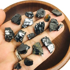 May include: A collection of black and silver raw, unpolished, rough, natural,  black tourmaline crystals. The crystals are various sizes and shapes.