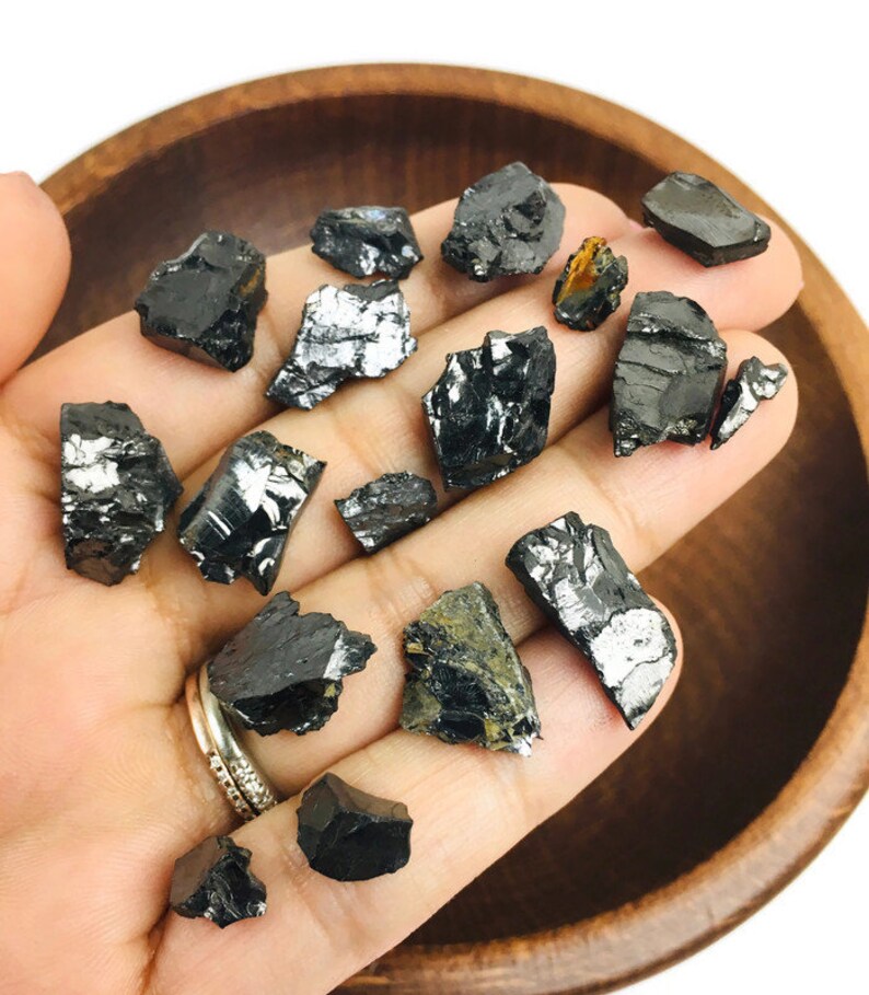 May include: A collection of black and silver raw, unpolished, rough, natural,  black tourmaline crystals. The crystals are various sizes and shapes.