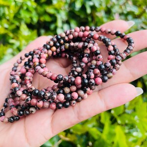 May include: A close-up of a stack of pink and black gemstone bracelets. The bracelets are made of small, round beads and are strung on elastic.
