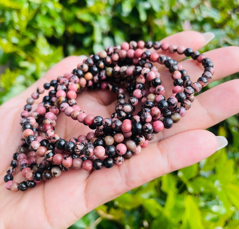 May include: A close-up of a stack of pink and black gemstone bracelets. The bracelets are made of small, round beads and are strung on elastic.