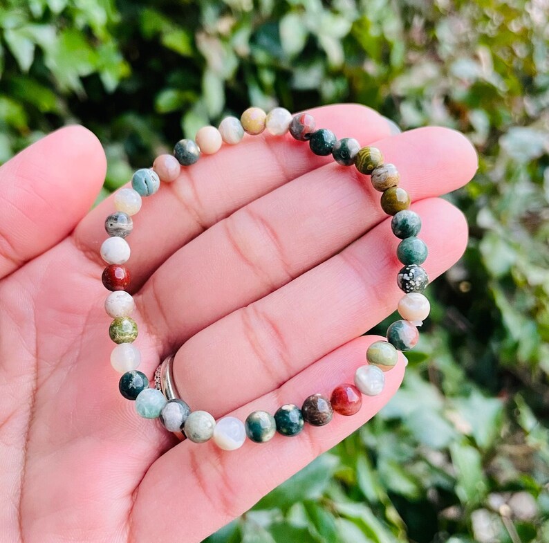 May include: A bracelet made of small, round, multi-colored stones. The stones are a mix of green, brown, red, and white.