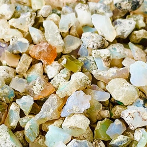 May include: A close-up of a pile of small, rough, white, and iridescent opal stones. The stones are various shapes and sizes, and some have a light blue or green hue.