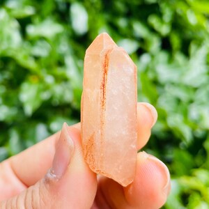 May include: A translucent, light pink crystal with a red stripe running through the center. The crystal is pointed at both ends and has a natural, rough texture.