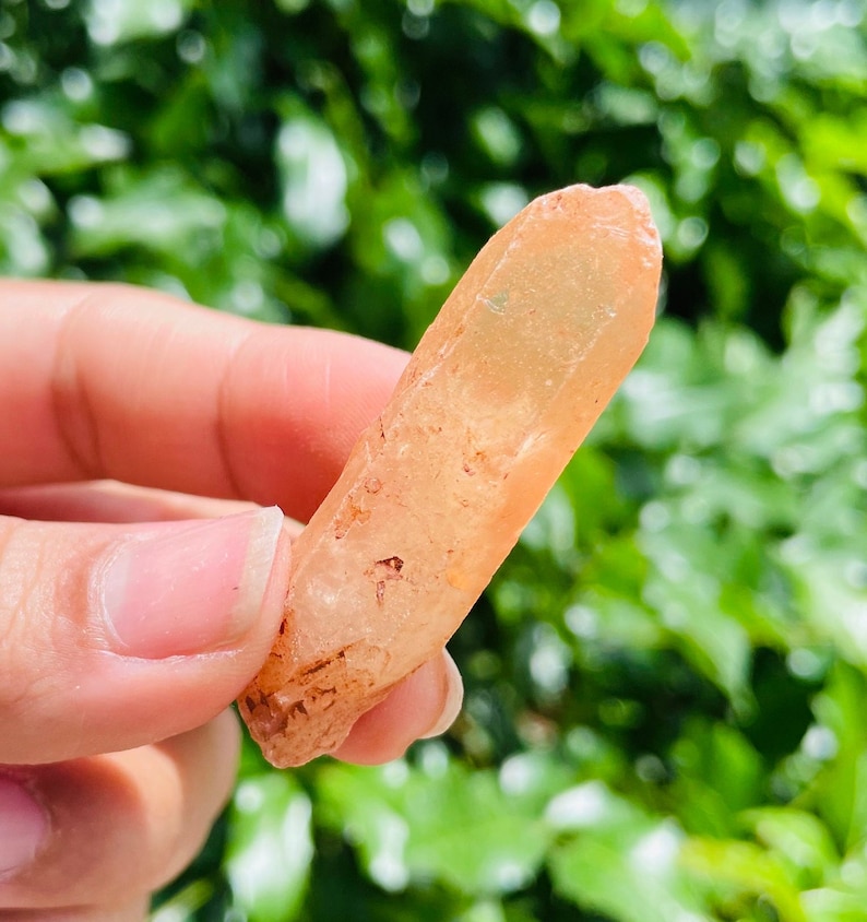 May include: A light orange crystal point with a clear, translucent body and a slightly rough texture. The crystal is pointed at one end and has a flat base.
