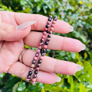 May include: A pink and black gemstone bracelet featuring small round beads. The bracelet is crafted from natural stones and is a beautiful and unique piece of jewellery.