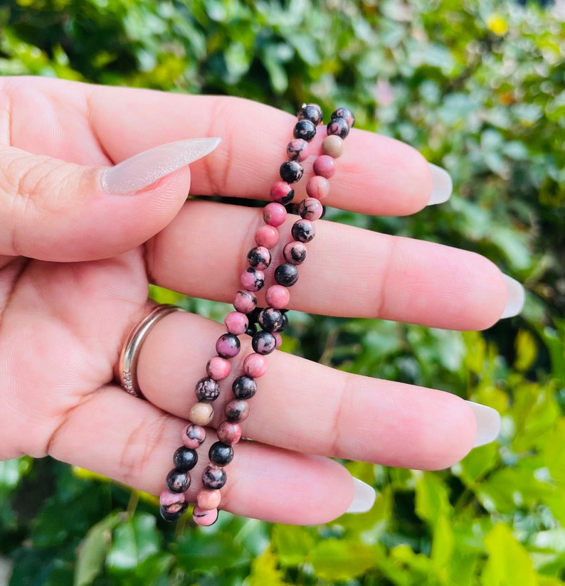 May include: A pink and black gemstone bracelet featuring small round beads. The bracelet is crafted from natural stones and is a beautiful and unique piece of jewellery.