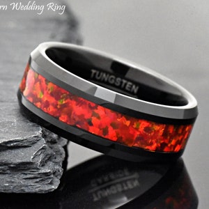 May include: A black tungsten wedding ring featuring a central inlay of vibrant red crushed opal. The interior of the band is clearly engraved with the word TUNGSTEN. The text Modern Wedding Ring is visible in the upper left corner of the image.