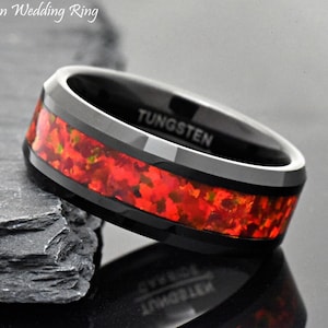 May include: A black tungsten wedding band with a red and gold inlay. The band is inscribed with the word "TUNGSTEN".