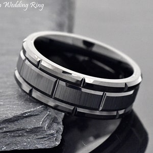 May include: A modern wedding ring with a black and silver design. The ring features a brushed black center band with a geometric pattern, framed by polished silver edges. The text "Modern Wedding Ring" is visible.
