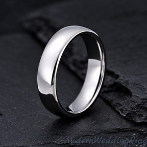 May include: A polished silver-toned metal ring with a smooth, rounded exterior surface and a simple, solid band design. The ring features a high-shine reflective finish that catches the light, creating bright highlights along the curved edges.