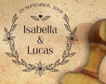 Könnte beinhalten: Ein Holz-Stempel mit einem floralen Kranz-Design und dem Text "28. SEPTEMBER 2019 Isabella & Lucas".