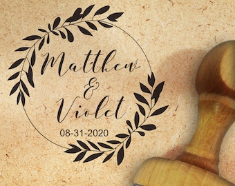 Könnte beinhalten: Ein Stempel aus Holz mit einem schwarzen Stempelkissen. Der Stempel zeigt einen Kranz aus Blättern mit dem Text "Matthew & Violet 08-31-2020" im Inneren.