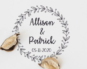 Könnte beinhalten: Ein weißer Hintergrund mit braunen getrockneten Blütenblättern, die um einen schwarzen und weißen, kundenspezifischen Gummistempel mit dem Text "Alison & Patrick 05-11-2020" in einem Kranzdesign verstreut sind. Der Text "love" ist in Kursivschrift auf einem Holzschild unter dem Stempel geschrieben.
