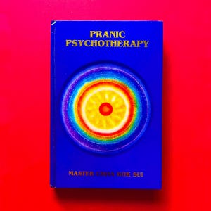 May include: A blue book titled "Pranic Psychotherapy" with gold lettering. The cover features a colorful circular design with a red center. The author's name, Master Choa Kok Sui, is printed at the bottom. The background is a solid red.