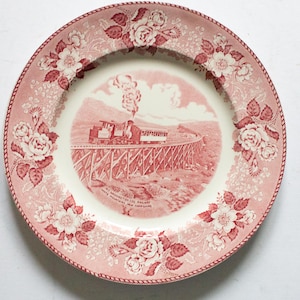 May include: A vintage ceramic plate with a red and white floral design. The central image is a red illustration of a train crossing a bridge. The plate has the text "MT. WASHINGTON CO'S. RAILWAY WHITE MOUNTAINS, NEW HAMPSHIRE."