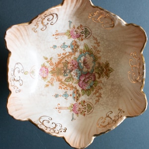 May include: A white ceramic bowl with a scalloped edge and a floral design in gold, pink, blue, and green. The bowl has a crackled glaze and a gold rim.