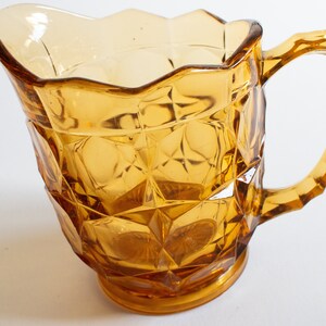 May include: Amber glass pitcher with a faceted design and a handle. The pitcher has a scalloped rim and a wide base.