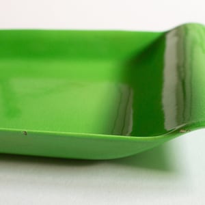 Puede incluir: Una bandeja de servir de cerámica verde brillante con un borde ondulado. La bandeja es brillante y tiene una ligera curva en la parte inferior.