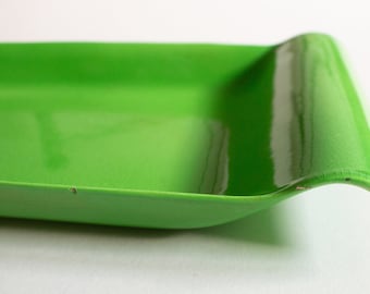 May include: A bright green ceramic serving tray with a wavy edge. The tray is glossy and has a slight curve to the bottom.