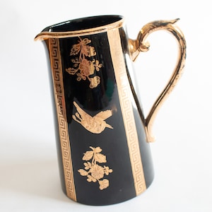 May include: Black ceramic pitcher with a gold handle and gold Greek key and floral designs.
