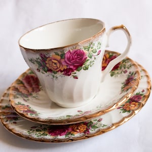 以下が含まれることがあります： ピンク、イエロー、グリーンの色の花柄が施された白いティーカップとソーサーのセット。セットは金色の縁取りと波状の縁取りが施されています。