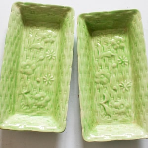 Op de afbeelding: Twee rechthoekige, lichtgroene keramische schalen met een mandweefseltextuur. Elke schaal heeft reliëf bloemen- en sterpatronen. De schalen hebben een iets verhoogde rand en zijn geschikt om te serveren of tentoon te stellen.