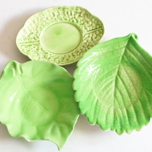 May include: Three ceramic dishes in shades of light green. One dish is oval with a textured border, while the other two are shaped like leaves with visible veins. The leaf-shaped dishes have a glossy finish, and one features a subtle crackle glaze.