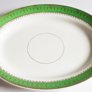 May include: Oval serving platter with a white centre and a green border. The green border is decorated with a gold leaf pattern. A gold circle is in the centre of the platter. The platter is a vintage piece.
