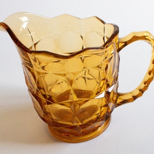 May include: Amber glass pitcher with a diamond pattern and a handle. The pitcher has a scalloped rim.