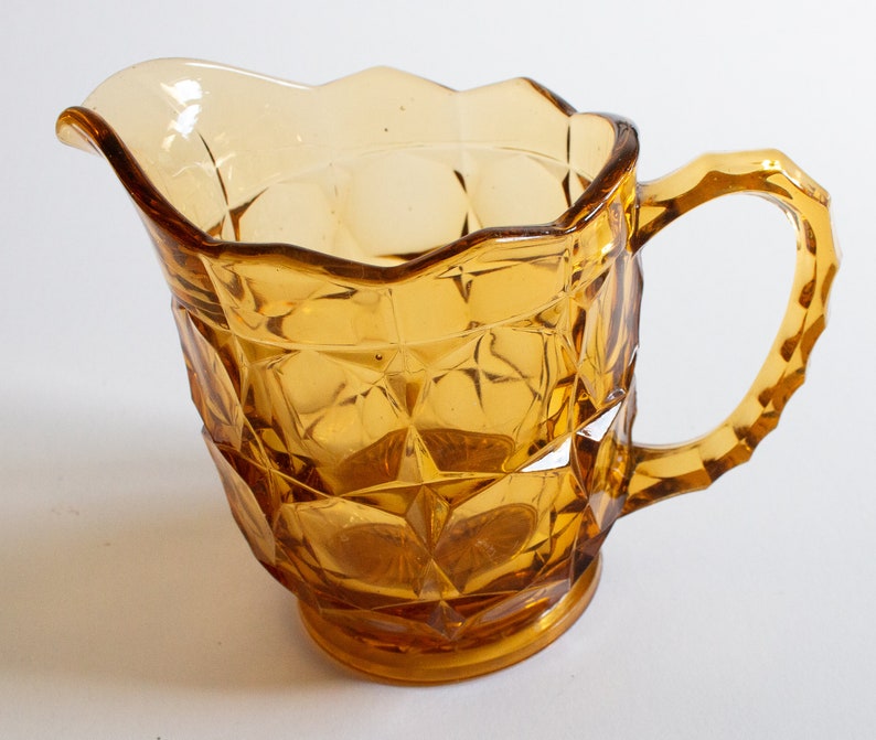 May include: Amber glass pitcher with a diamond pattern and a handle. The pitcher has a scalloped rim.