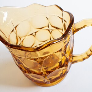 May include: Amber glass pitcher with a faceted design and a handle. The pitcher has a wide mouth and a rounded base.