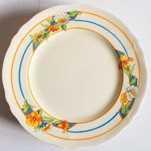 May include: A white ceramic plate with a blue and yellow floral design. The plate has a scalloped edge and a raised rim.