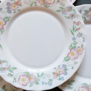 May include: A set of white ceramic plates with a floral design featuring pink, blue, and green flowers. The plates have a scalloped edge.