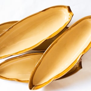 Puede incluir: Conjunto de cuatro platos de servir de cerámica de color marrón claro. Los platos tienen forma de hojas de plátano y tienen un borde ligeramente ondulado.