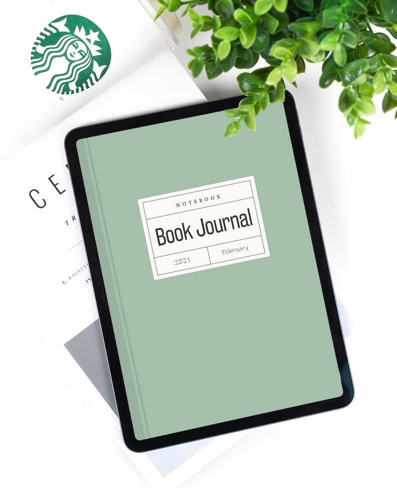 May include: A green digital tablet with a black frame displaying a book journal cover. The cover has a white label with the text "Notebook Book Journal" and the dates "2021" and "February".