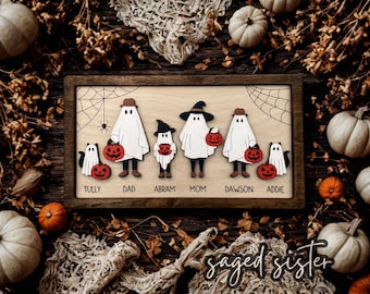 Puede incluir: Un letrero familiar de Halloween enmarcado en madera con figuras de fantasmas sosteniendo calabazas. El letrero incluye los nombres Tully, Dad, Abram, Mom, Dawson y Addie. El fondo está decorado con calabazas, hojas y telarañas.