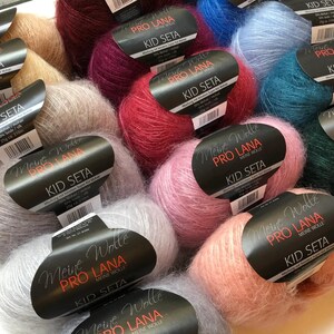 May include: A selection of colourful yarn skeins in various shades, such as pink, red, blue, and grey. Each skein is labelled "Kid Seta" and "Meine Wolle Pro Lana". The yarn has a soft, fluffy appearance, suitable for knitting or crochet.
