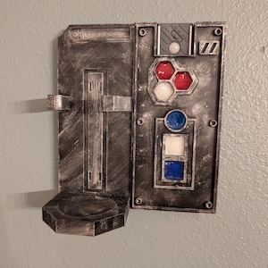 May include: A weathered, metallic-looking wall-mounted panel with a hinged section and a small shelf. The panel features various colored geometric shapes, including red, white, and blue, and a series of rectangular and circular elements. The overall design suggests a sci-fi or industrial aesthetic.