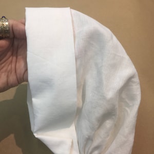 May include: A white linen fabric hat with a gathered elastic band at the bottom.