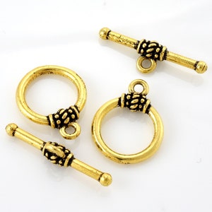 May include: Three gold-toned metal toggle clasps with decorative accents. The clasps are designed for jewelry making and feature a round ring and a bar with a decorative end.