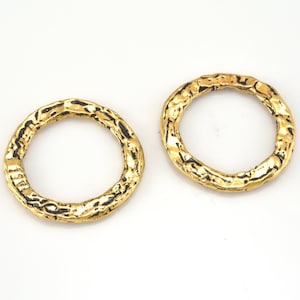May include: Two gold-toned metal rings with a textured surface. The rings are round and have a smooth inner edge.