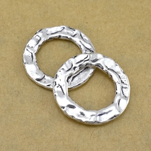 May include: Two silver-toned metal rings with a textured surface. The rings are interlocked and have a circular shape.